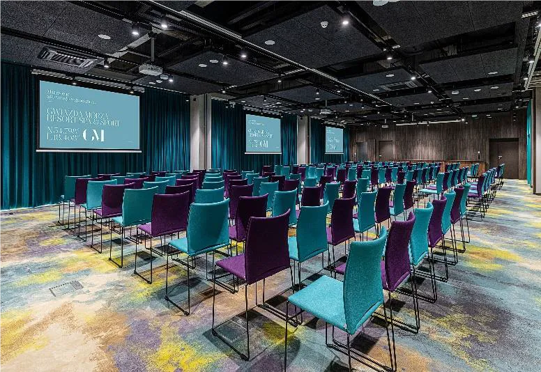 Sala konferencyjna przygotowana na Walne Zgromadzenie Izby Branży Komunalnej 10 czerwca 2022 r., z rzędami turkusowych i fioletowych krzeseł skierowanych w stronę dwóch ekranów projekcyjnych.