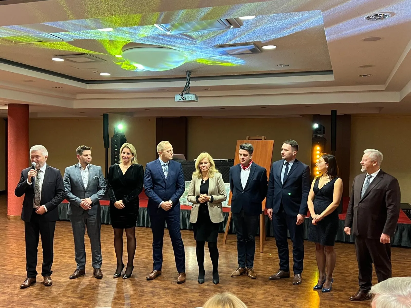 Grupa uczestników I Zjazdu Szkoleniowo-Integracyjnego Izby Branży Komunalnej stoi w szeregu w sali konferencyjnej, a jedna z osób przemawia do mikrofonu.