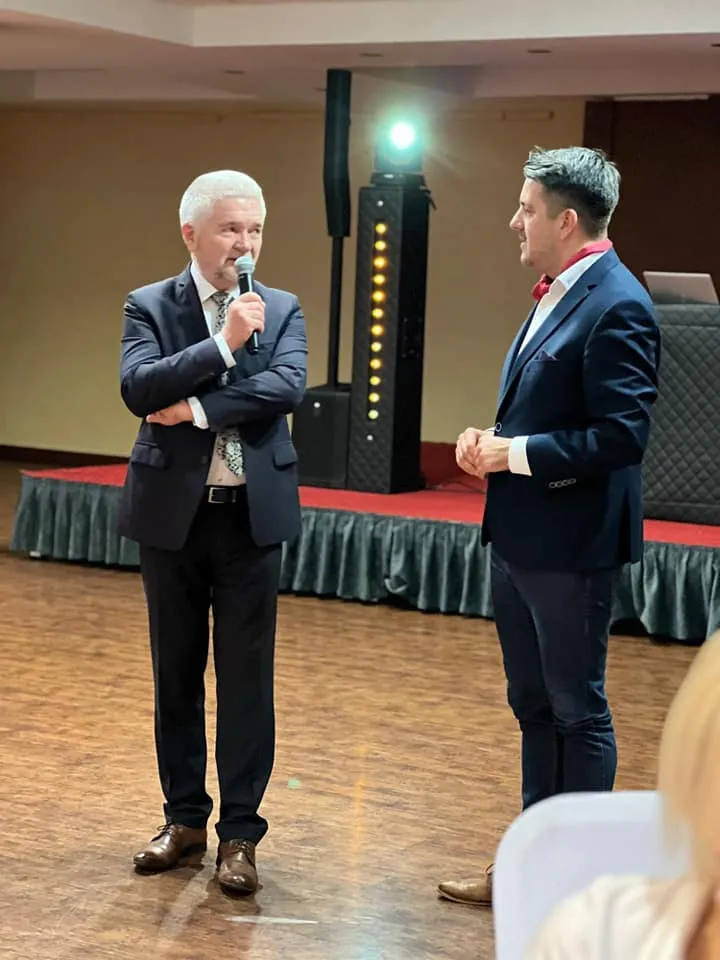 Dwóch mężczyzn w garniturach stoi na sali konferencyjnej podczas I Zjazdu Szkoleniowo‑Integracyjnego Izby Branży Komunalnej, a jeden z nich przemawia do mikrofonu.