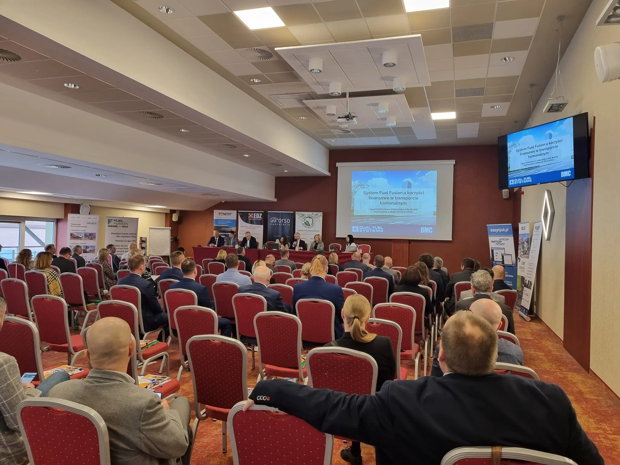 Uczestnicy I Zjazdu Szkoleniowo-Integracyjnego Izby Branży Komunalnej siedzą w sali konferencyjnej i słuchają prezentacji wyświetlanej na ekranie.