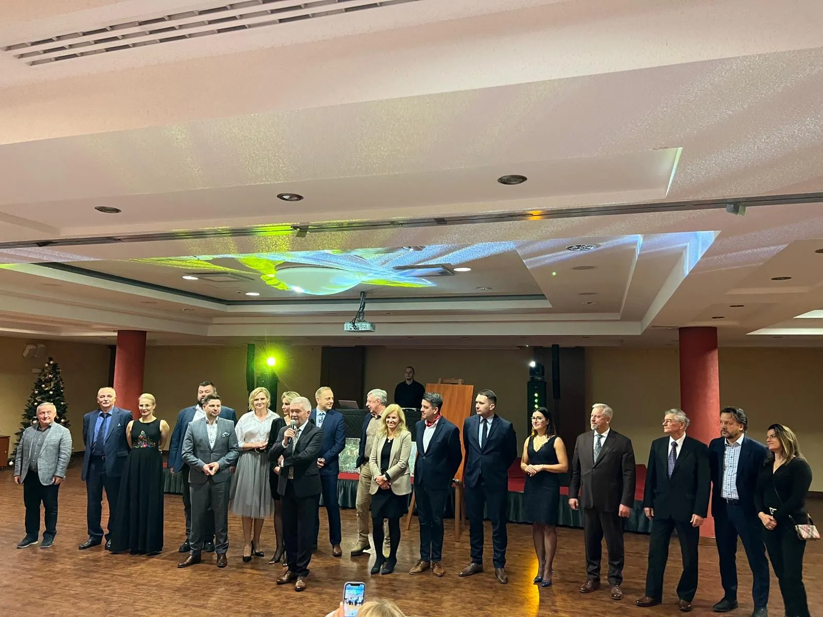 Grupa uczestników I Zjazdu Szkoleniowo-Integracyjnego Izby Branży Komunalnej stoi w jednym rzędzie na sali konferencyjno-bankietowej podczas oficjalnej części wydarzenia.