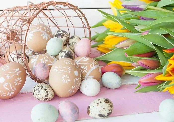 Wielkanocna kompozycja z kolorowymi pisankami wysypującymi się z koszyczka i bukietem tulipanów na pastelowym tle.