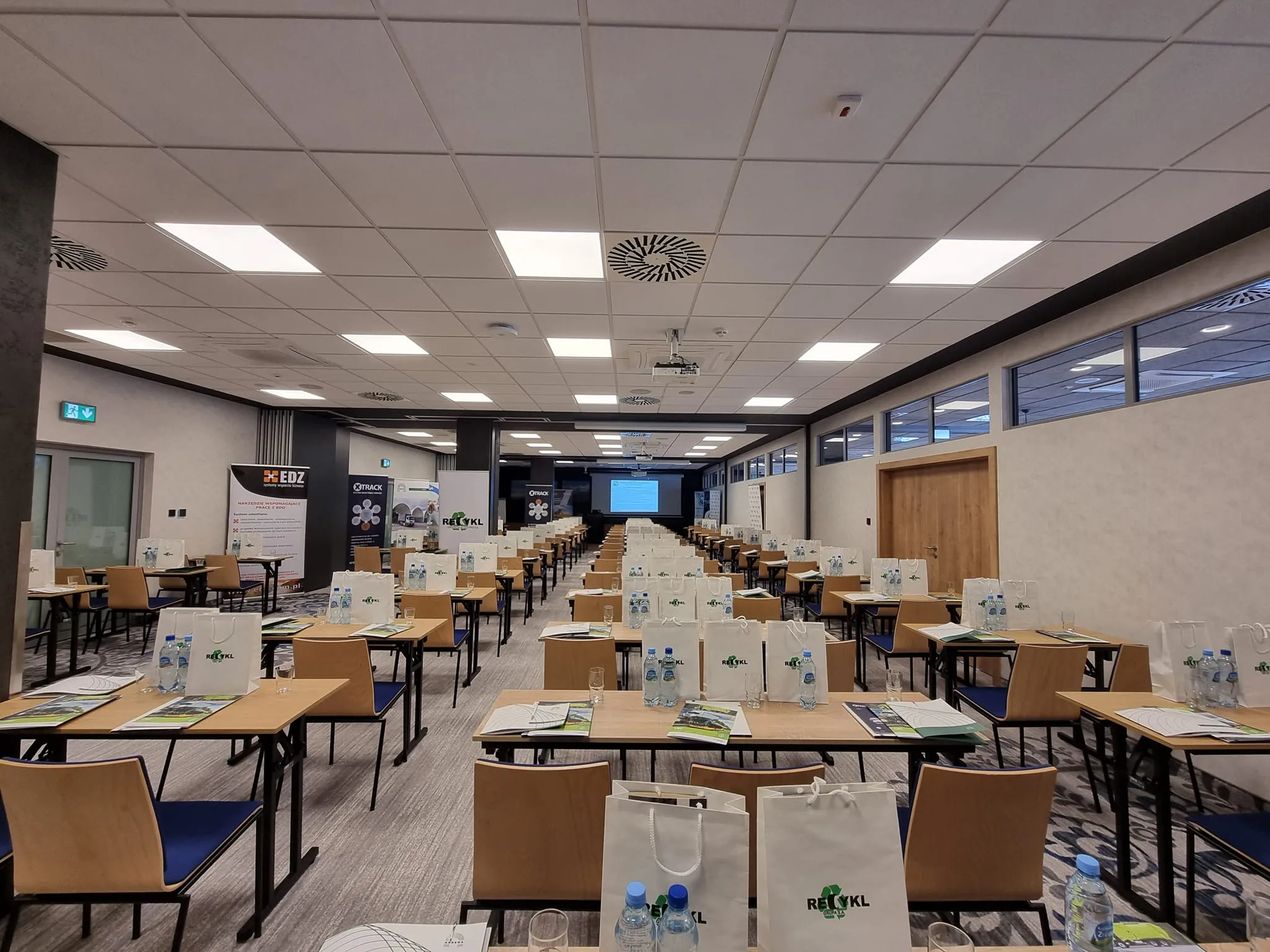 Sala konferencyjna przygotowana na II Zjazd Szkoleniowo‑Integracyjny, z rzędami stołów, krzeseł i materiałami dla uczestników.