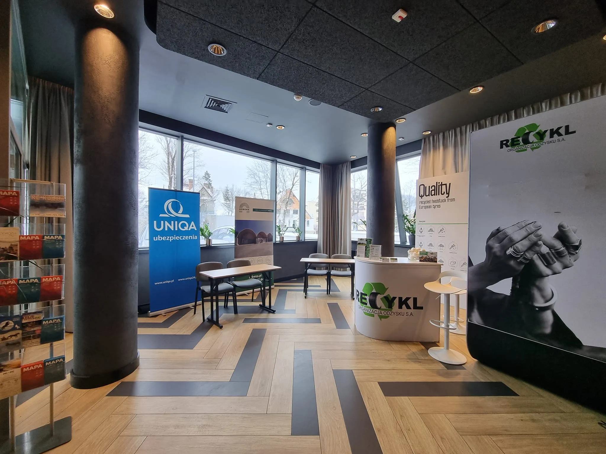 Stoisko wystawiennicze partnerów II Zjazdu Szkoleniowo‑Integracyjnego z roll‑upami firm i ladą informacyjną w nowoczesnym, jasnym holu konferencyjnym.