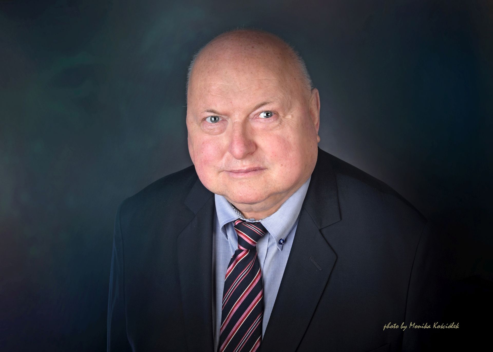 Portret starszego mężczyzny w garniturze i krawacie na ciemnym tle, wykonany w stylu oficjalnym.